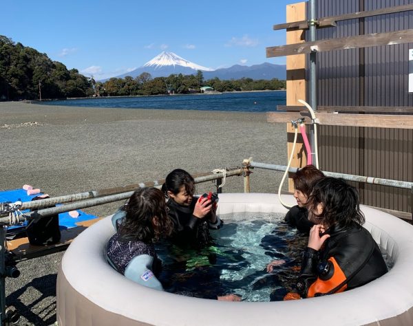 富士山バックに海辺の簡易お風呂でダイバー4人がくつろいでる写真