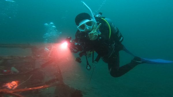 ライトもったダイバーがカメラ目線でピースサインしている写真