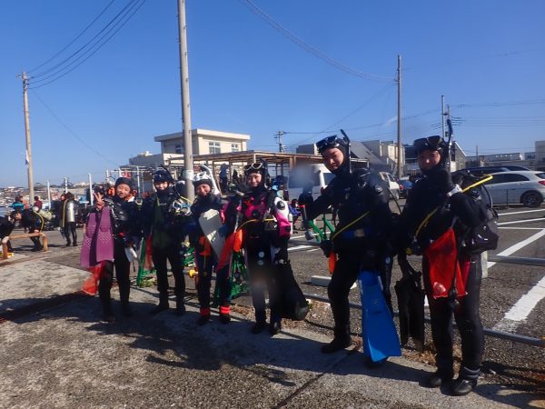 ダイビング器材を背負った6人のダイバーが潜る前に写真を撮っている写真