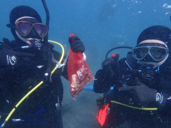 海底のごみを集めたごみ袋を指さしてポーズをとるダイバー2人の写真