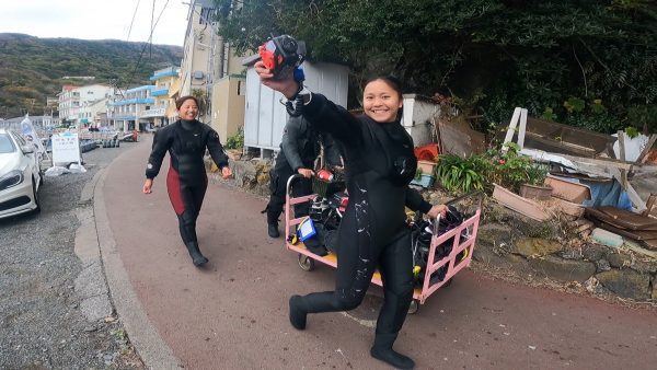 器材を乗せた台車をダイビングスーツ着たダイバーが押している写真。